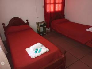 Habitación con 2 camas, sábanas rojas y toallas blancas. en Hosteria La Farfalla en Chos Malal