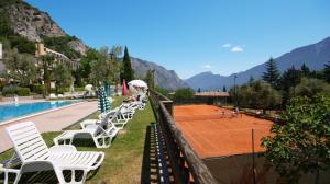 a tennis court with white chairs next to a pool at Village Bazzanega - Montagnoli Group in Tremosine Sul Garda
