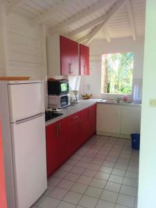 a kitchen with red cabinets and a white refrigerator at Maison charmante à Sainte-Rose + Piscine in Sainte-Rose