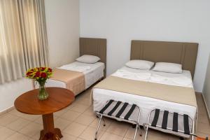twee bedden in een kamer met een tafel en een vaas met bloemen bij Bandeirantes Hotel in Cuiabá