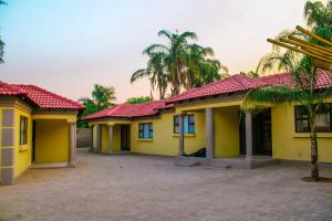 a yellow house with red roofs and palm trees at Maruleng Guest House in Hoedspruit