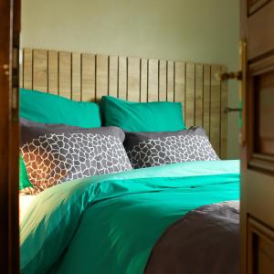 Schlafzimmer mit einem Bett mit grüner Bettwäsche und Kissen in der Unterkunft COTTAGE-GITE COEUR DE SUNDGAU in Leymen