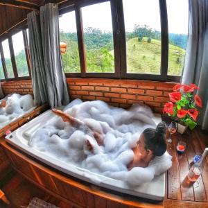 une femme posant dans un bain moussant dans une pièce avec fenêtre dans l'établissement Chalés Kalanchoe, à Visconde de Mauá