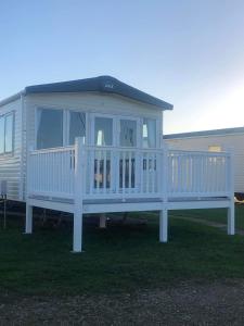 une maison blanche avec une terrasse couverte sur la pelouse dans l'établissement holidayhome-romneysands holiday park, à Littlestone-on-Sea
