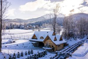 una cabaña de madera en la nieve con montañas en el fondo en udanypobyt Domki Przy Potoku, en Zakopane