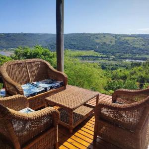 2 sillas de mimbre y una mesa en una terraza de madera en African Sunset Villa, en Chintsa