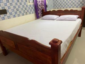 uma cama de madeira com lençóis brancos e almofadas em Sarah Residency em Thanjavur