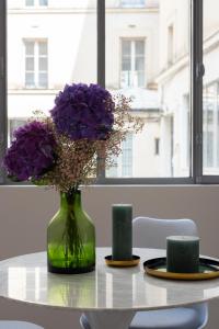 a green vase with purple flowers sitting on a table at Mayenne in Paris