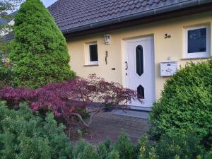 una casa amarilla con una puerta blanca y algunos arbustos en Heideperle3a en Mönchhagen