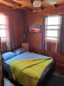 a bedroom with a bed with yellow sheets and windows at Mx2 Cottage in Calibishie