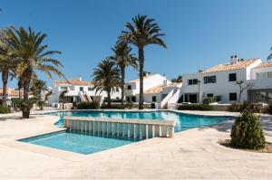 a swimming pool with palm trees and white buildings at Tranquilo apartamento. Piscina, playa y relax. in Sa Caleta