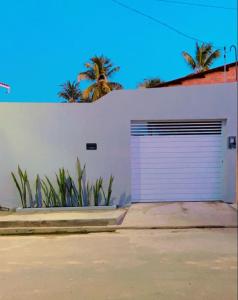 a white garage door with palm trees in the background at Casa em São Miguel dos milagres. in São Miguel dos Milagres