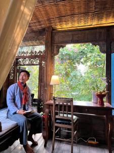 
a man sitting on a bed in front of a window at Baan Boo Loo Village- SHA Plus in Chiang Mai
