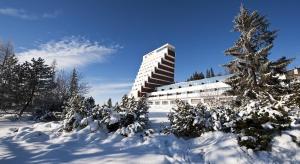 a snow covered yard with a building and a tree at Hotel Panorama Resort in Vysoke Tatry - Strbske Pleso