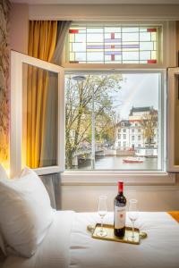 Una botella de vino y dos copas en una cama con ventana en Hotel Oscar, en Ámsterdam