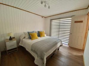 Un dormitorio con una cama con almohadas amarillas y una ventana en Cabañas Los Robles, en Coelemu