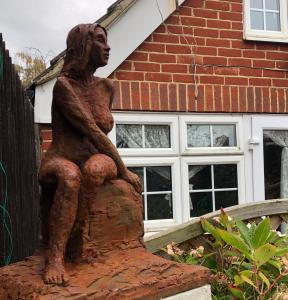 a statue of a woman sitting on a fence at The Artist’s Hideaway. in Woking