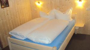 uma cama com lençóis brancos e almofadas em Pension Sursilva em Gargellen