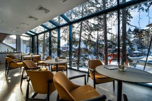 um restaurante com mesas e cadeiras e janelas grandes em Mona Plaza Zlatibor em Zlatibor