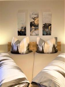 two pillows on a bed with three paintings on the wall at Ferienwohnungen Sernatinger in Bad Reichenhall