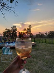 una persona sosteniendo una copa de vino con la puesta de sol en el fondo en Chacra mita í, en La Cruz