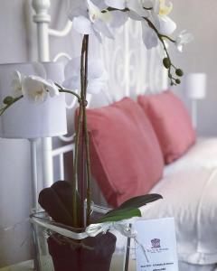 un vaso con fiori bianchi su un tavolo accanto a un letto di Il Tempio di Athena - Cultura e Relax a Siracusa a Siracusa