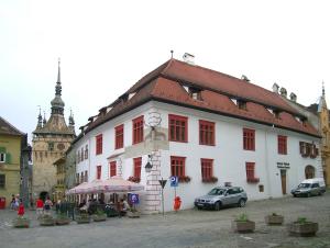 a white building with red windows in a street at Casa cu Cerb in Sighişoara