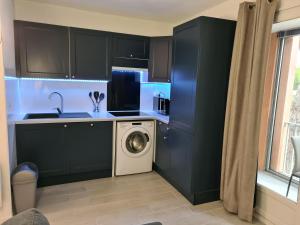 a kitchen with black cabinets and a washing machine at Superbe T2 climatisé, proche plage avec parking privé in Saint-Cyprien