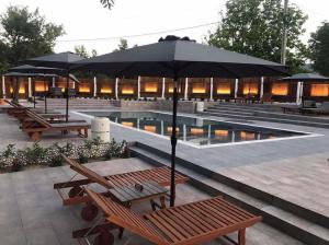 a pool with benches and umbrellas next to a pool at Семеен хотел и ресторант Райски залив in Golyama Zhelyazna