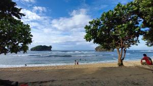 a beach with a tree and people on the beach at MIN Guest House Watukarung in Pacitan