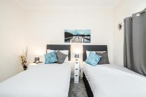 Duas camas num quarto com paredes brancas e almofadas azuis em MPL Apartments - Malden Road Serviced Accommodation em Watford