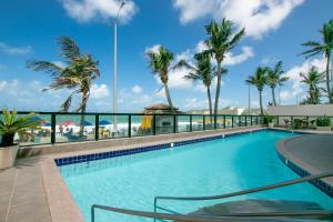 a swimming pool with palm trees and the ocean at Kings Flat - Apartamentos com conforto beira mar in Natal