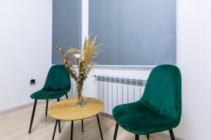 zwei grüne Stühle und ein Tisch mit einer Vase drauf in der Unterkunft VODNA White Apartment in Lwiw