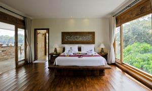 a bedroom with a large bed and large windows at Sri Ratih Cottages, CHSE Certified in Ubud