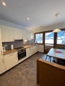 a kitchen with white cabinets and a table and a dining room at Ferienwohnungen Bailom in Elbigenalp