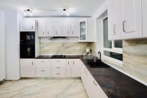 a white kitchen with white cabinets and black appliances at VILA COCA Sibiu in Sălişte