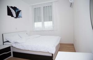 a white bedroom with a bed and a window at Sofija Apartment in Kumanovo