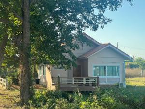 a small white house with a porch next to a tree at ทุ่งดินดำ Farm Stay in Ban Kho Wang