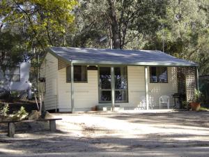 uma pequena casa branca com um banco à frente em Lakes Bushland Caravan & Lifestyle Park em Nicholson