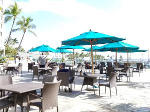 un grupo de mesas y sillas con sombrillas azules en Ilikai Tower 1 Bedroom City View Condos with Private Lanai & Free Wifi! en Honolulu