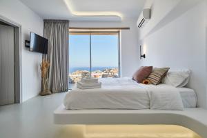 ein weißes Schlafzimmer mit einem großen Bett und einem großen Fenster in der Unterkunft Teal Rock Mykonos in Ano Mera