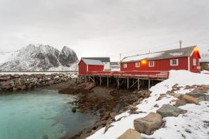 um edifício vermelho num cais junto a um rio em Olenilsøy Cabins em Reine