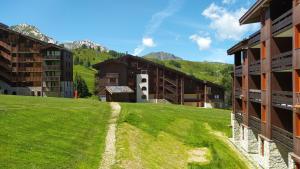 a grassy field next to some buildings with mountains at PARADISKI-BELLE PLAGNE, Altitude 2050m, APPART skis aux pieds 4 personnes in La Plagne Tarentaise