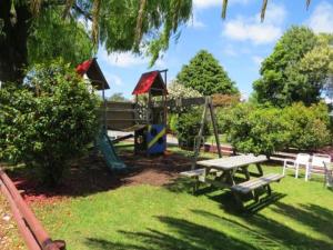 a park with a playground with a bench and a swing at Camellia Court Family Motel in Taupo