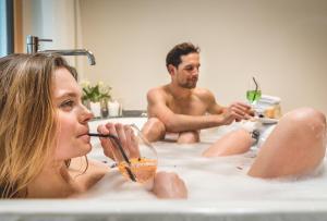 Un uomo e una donna in una vasca da bagno che bevono di TRAUBE BRAZ Alpen Spa Golf Hotel a Bludenz