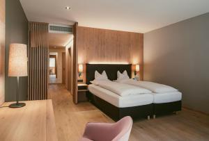 a bedroom with a large bed and a pink chair at TRAUBE BRAZ Alpen Spa Golf Hotel in Bludenz