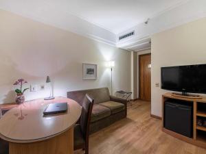 a living room with a table and a couch and a television at Hotel Cassino Tower Campinas Cambuí By Nacional Inn in Campinas