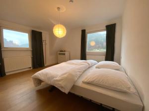 a bedroom with a bed with white sheets and two windows at Ferienhaus Waldglück in Calw