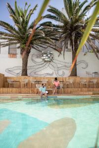 two people sitting next to a swimming pool with palm trees at Selina Punta Del Este in Punta del Este