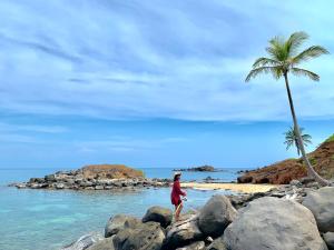 a woman walking on a rocky beach with a palm tree at ENSUEÑOS Natural Reserve Big House in Little Corn Island
